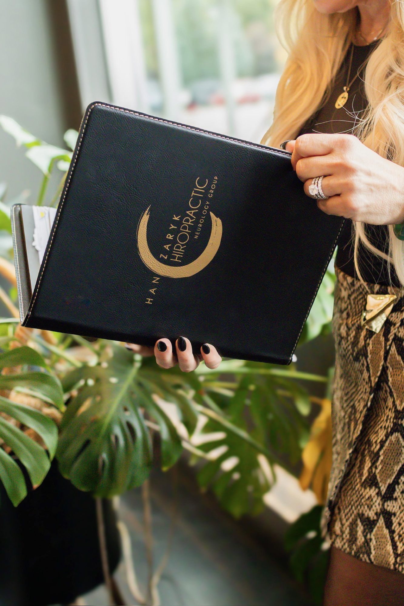 Dr. Christine holding the black HCNG patient folder beside a monstera