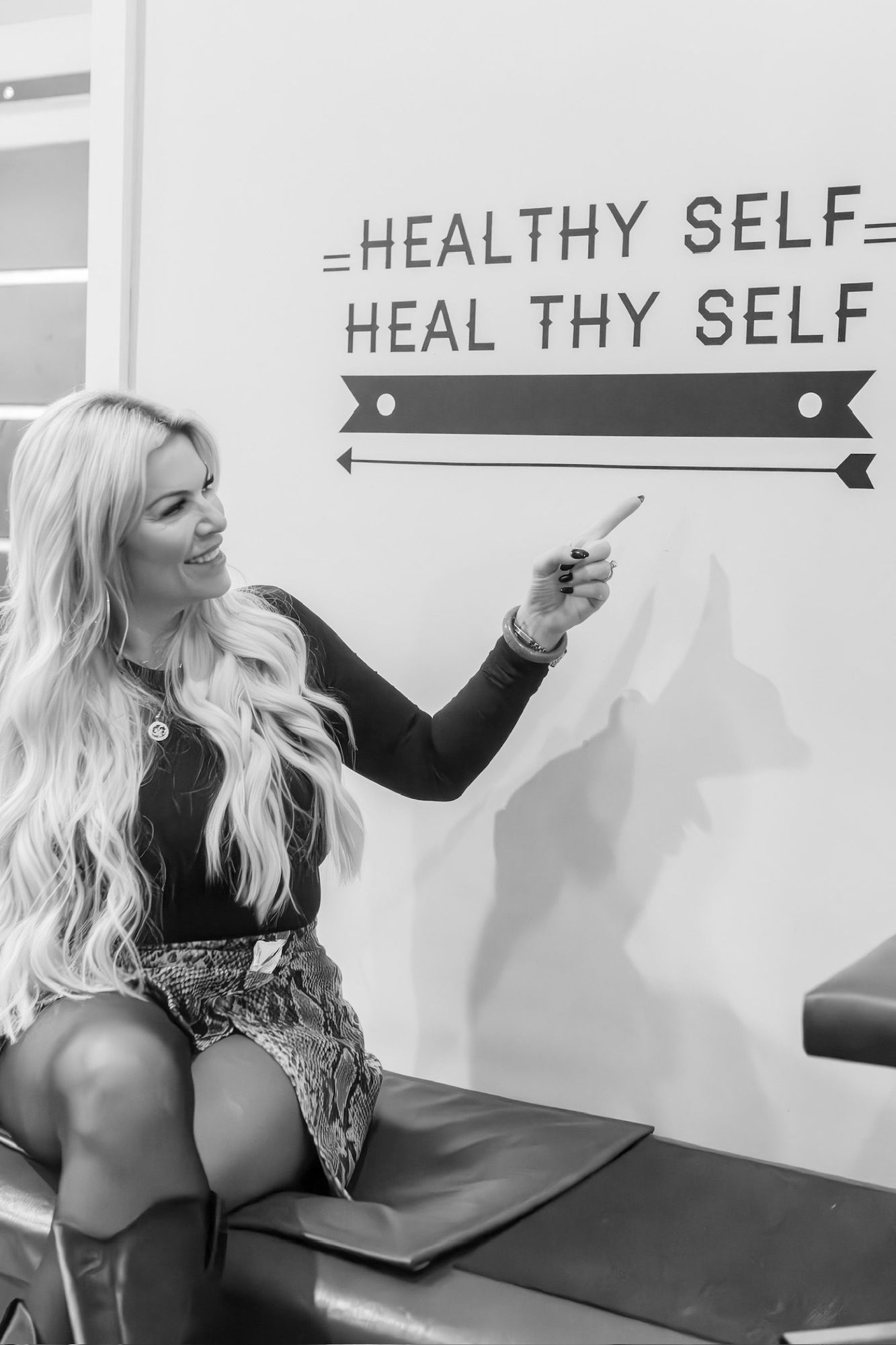 Dr. Christine pointing at the Healthy Self Heal Thy Self sign, in black and white