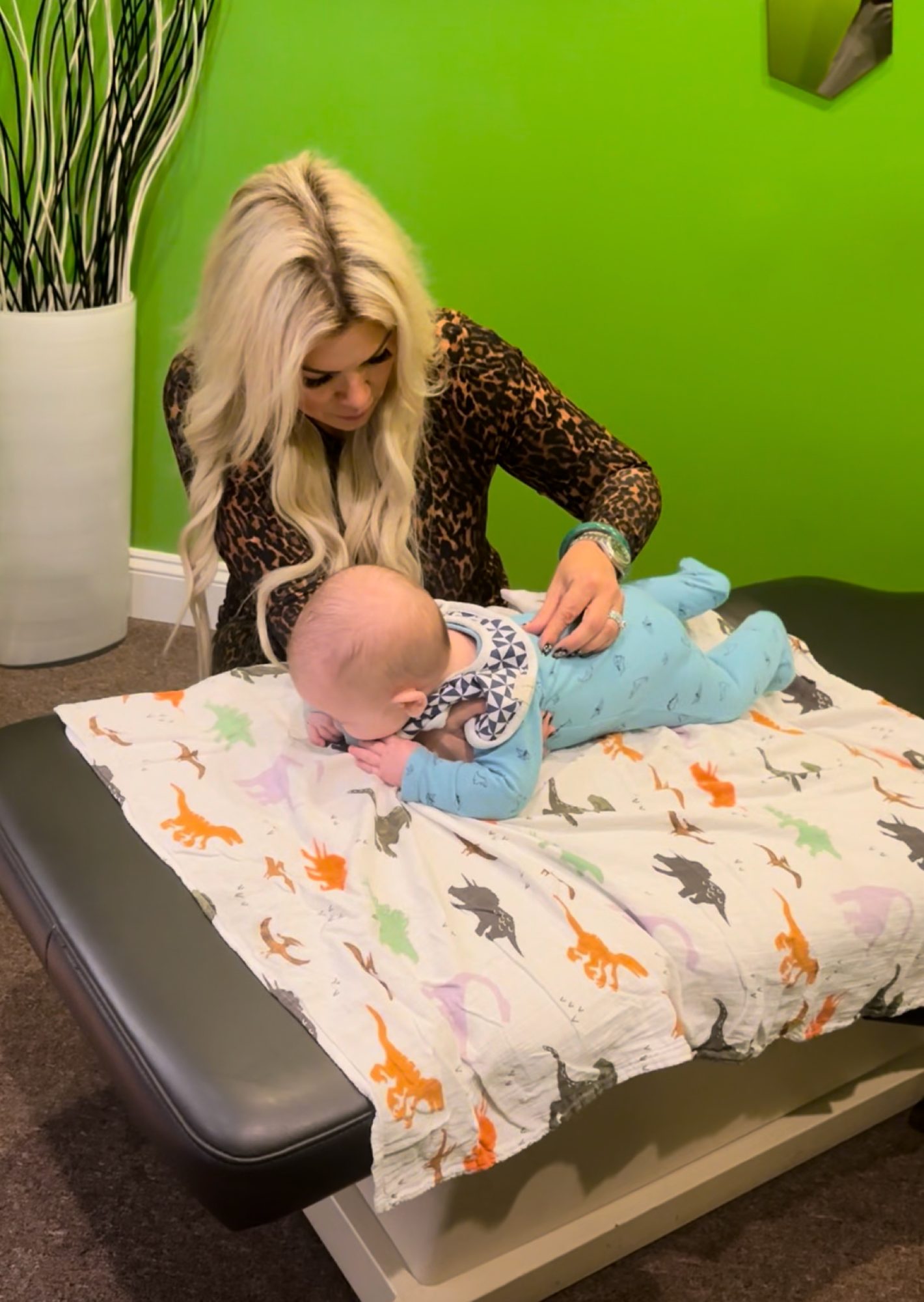 Dr. Christine gently checking a baby on a dinosaur blanket in the green kids room
