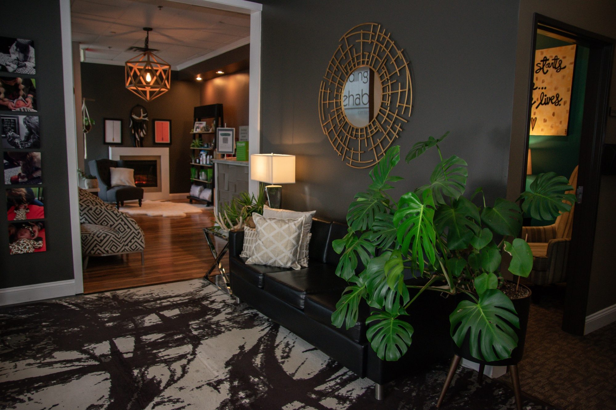 The reception room: black leather sofa, monstera, the brass sunburst mirror, and the fireplace room beyond